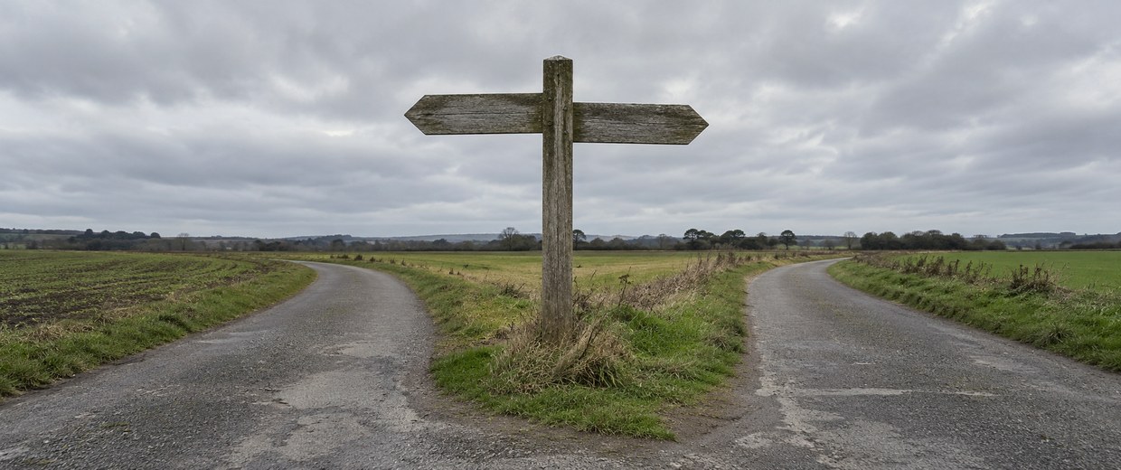 A weathered signpost at a fork in an empty road